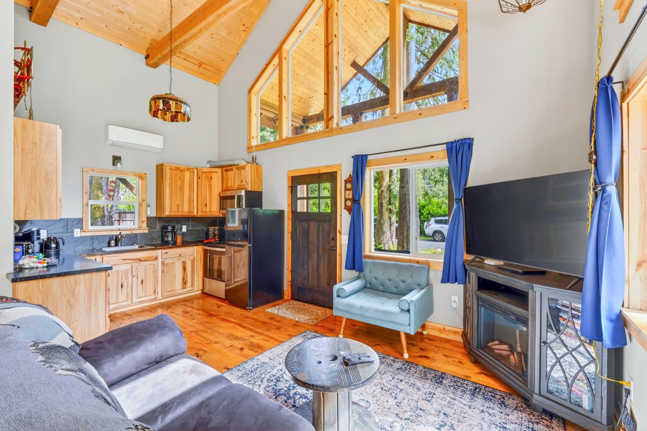 One big room: kitchen, dining, fireplace, and forest windows.